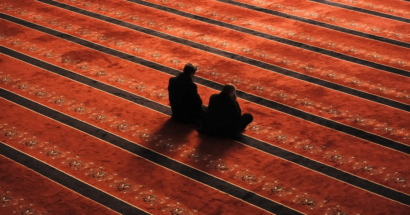Desenli kırmızı cami halısı üzerinde oturan iki kişinin yukarıdan görünümü